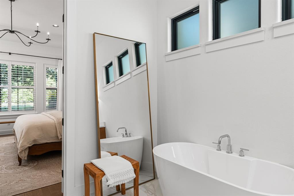 Primary bath soaking tub with floor-length gold mirror and clerestory windows